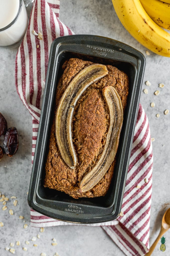 overhead image of banana bread in a pan styled with fruit and towel 