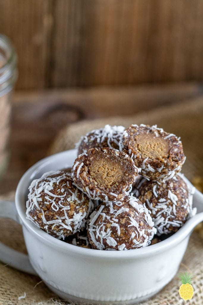 Image of chocolate banana peanut butter bliss balls in cup with two balls cut open. 