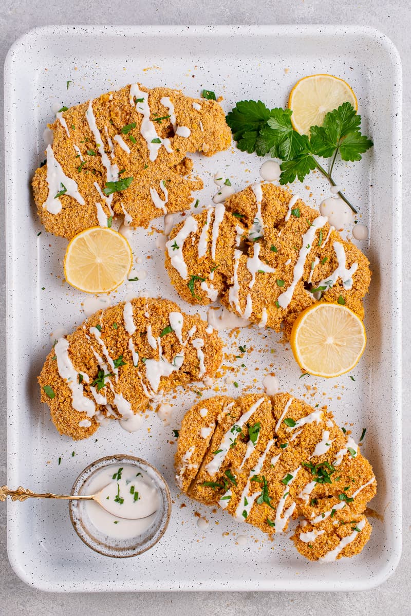 Breaded Cauliflower Steaks on white tray with sauce and parsley