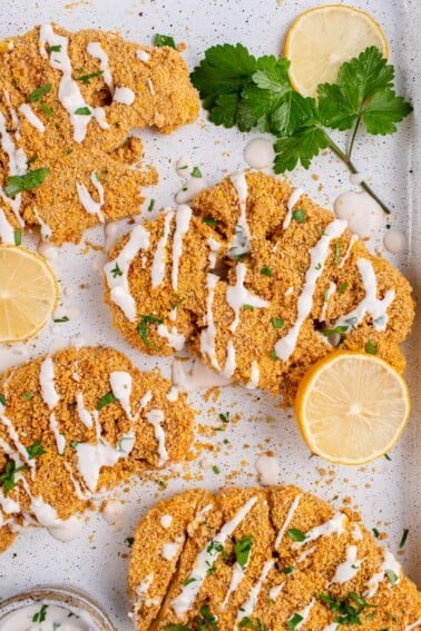 Breaded Cauliflower Steaks on white tray with sauce and parsley
