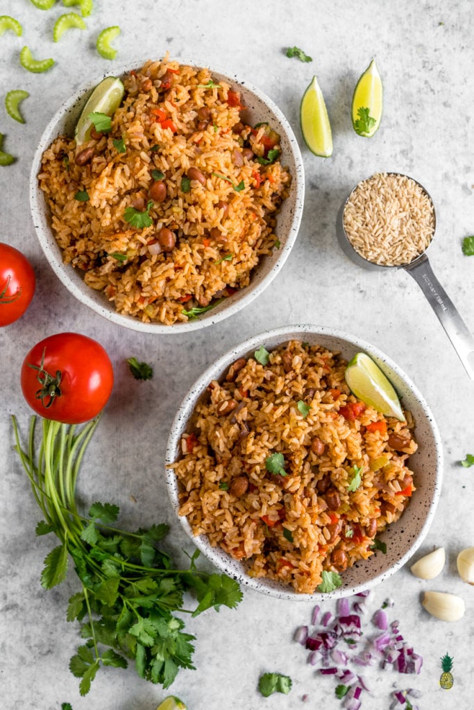 overhead image of spanish rice and beans in bowls styled with vegetables on light grey background. 