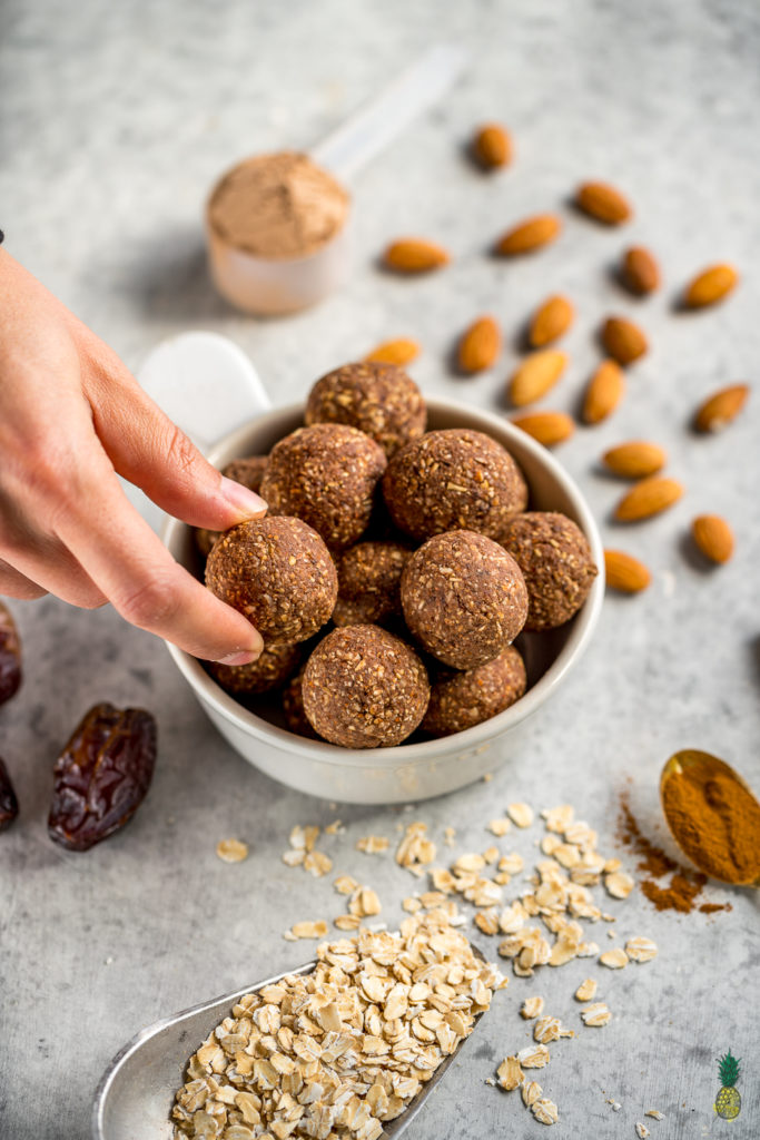 Bowl of bliss balls with a hand grabbing one on styled background. 