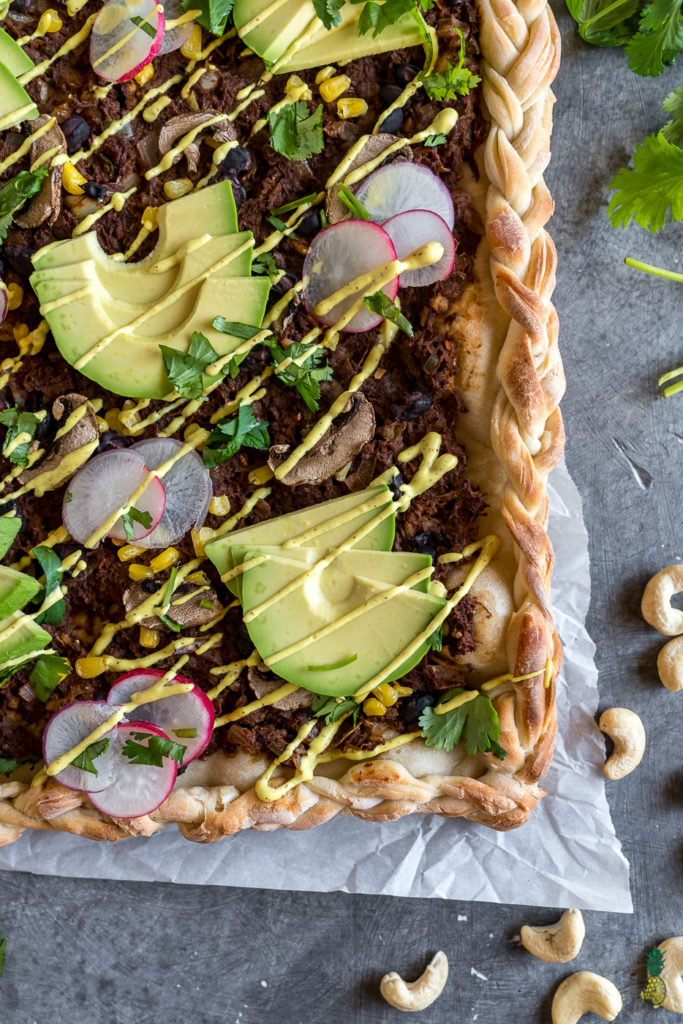 The perfect pizza topped with jackfruit smothered in mole sauce and topped with mushrooms corn, radish, avocado, and a cashew mustard cream sauce! #jackfruit #mole #vegan #pizza #entree #recipe #lunch #dinner #avocado #challenge #easy #mexican #unique #tacopizza