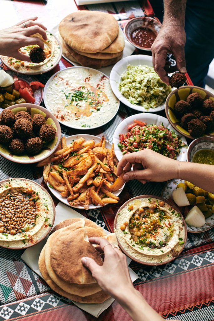 Image of falafel, hummus, and pita with hands grabbing food. 
