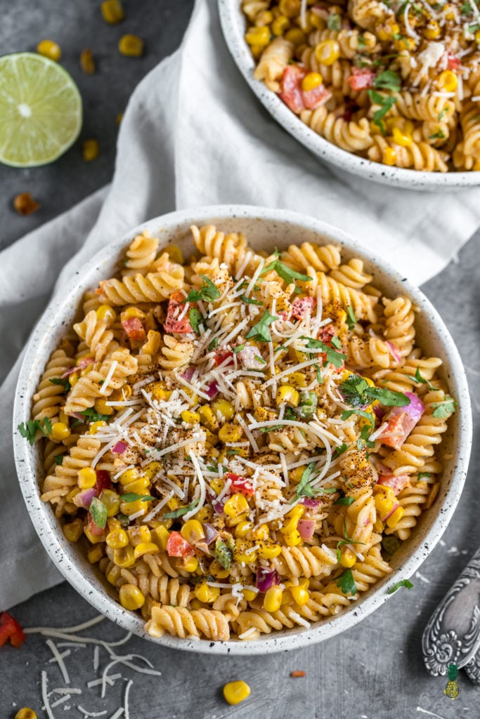 Close up shot of street corn pasta salad in a ceramic bowl with vegan parmesan cheese and spiral noodles