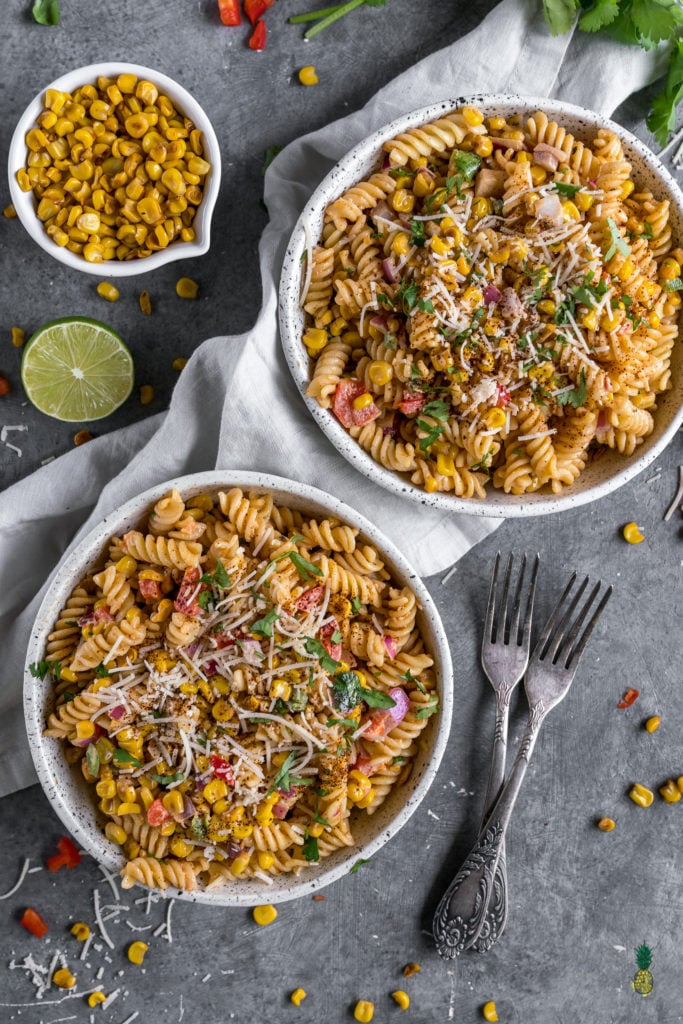 mexican street corn pasta salad in two bowls with garnishes and forks