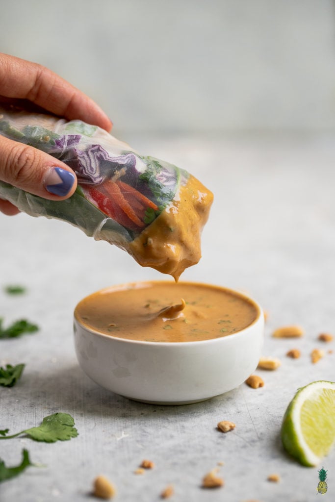 up close shot of spring roll being dipped in peanut sauce. 