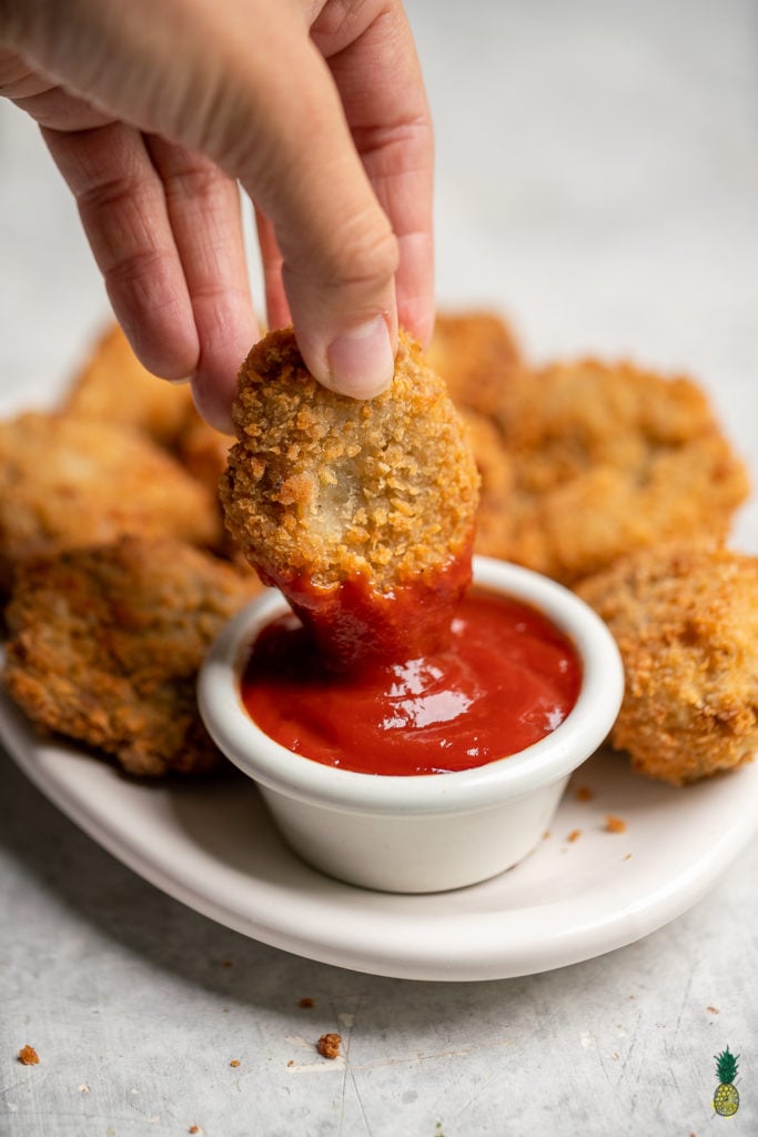 vegan chicken nugget being dipped in ketchup. 