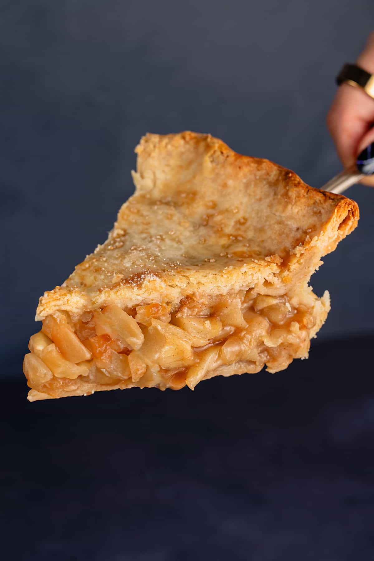 Slice of apple pie held up in front of blue backdrop
