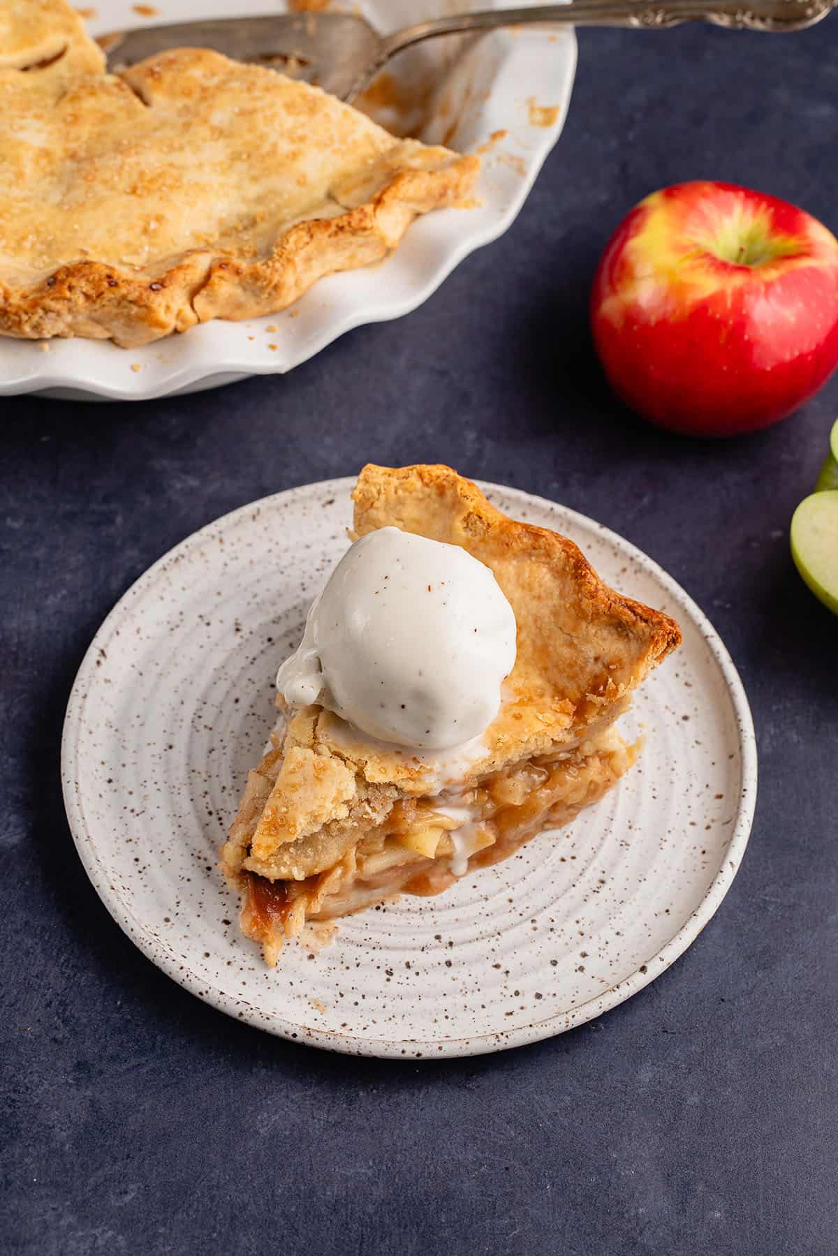 slice of vegan apple pie with vanilla ice cream on white plate
