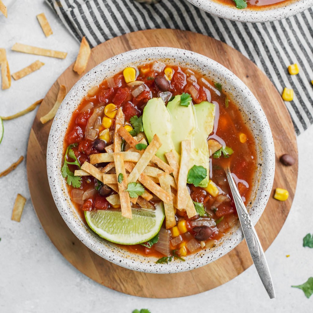 A bowl of vegan tortilla soup with garnishes and a spoon