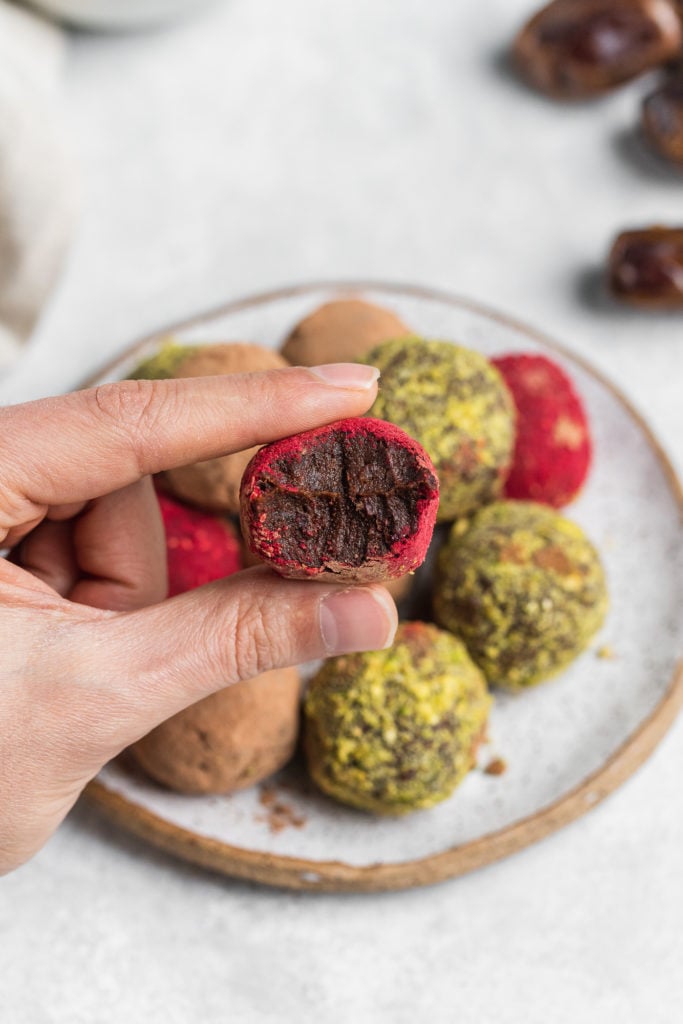 hand holding a biten into colorful vegan truffles on a serving plate