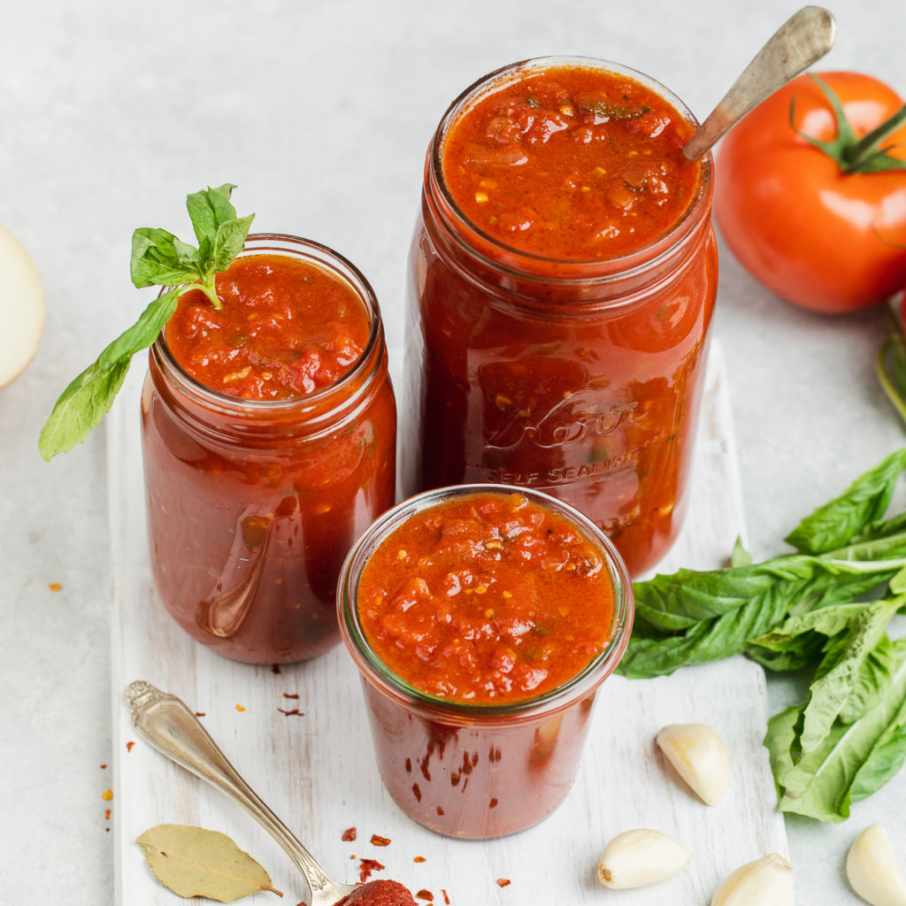 Homemade marinara sauce in jars with the ingredients and white background