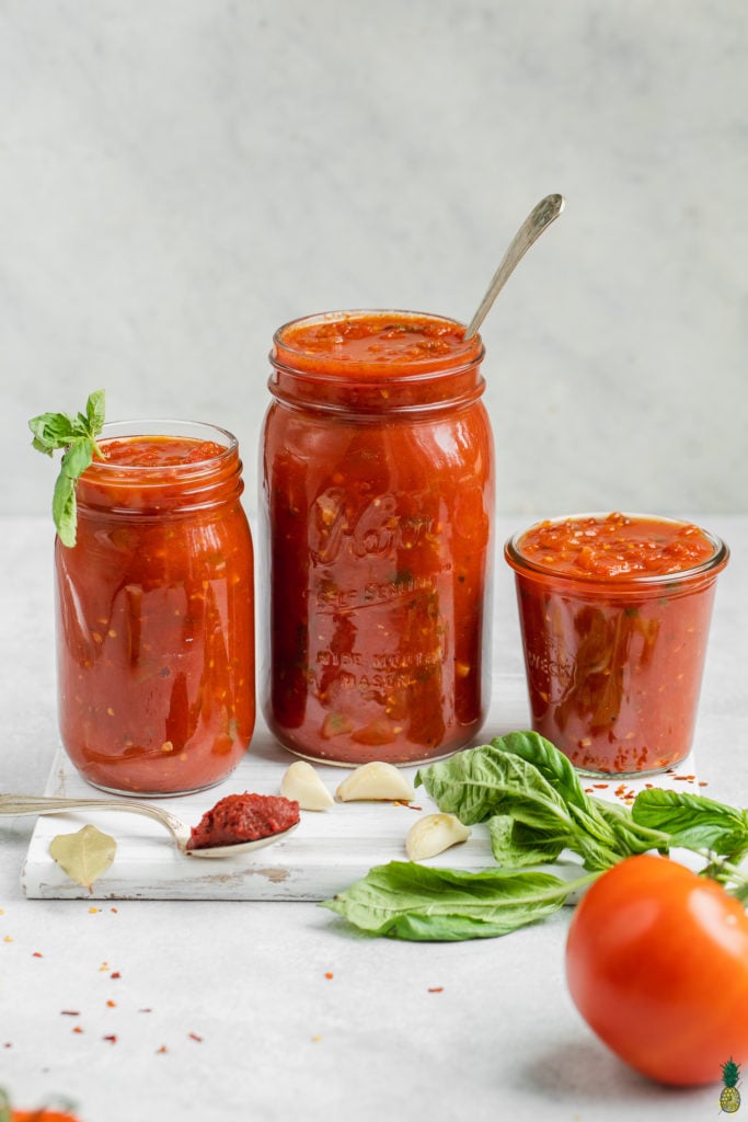 Homemade marinara sauce in jars with the ingredients and white background