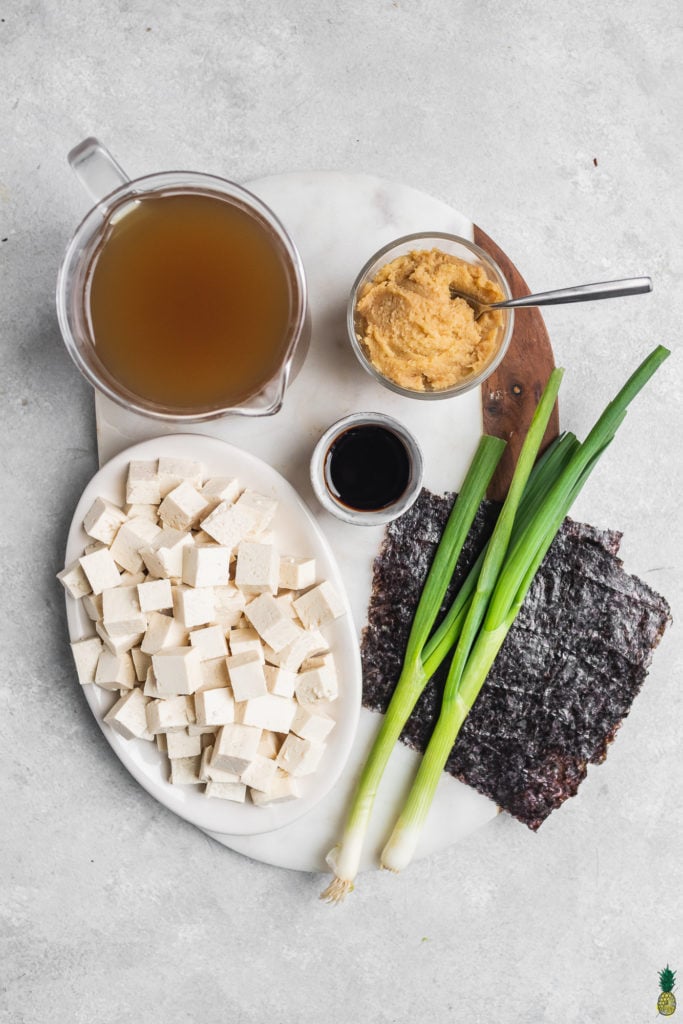 Ingredients for vegan miso soup, miso paste, vegetable broth, tofu, nori, green onions and soy sauce