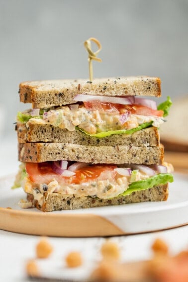 sliced vegan tuna salad sandwich with lettuce tomatoes and onion on a white plate