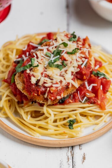 Vegan chicken parmesan garnished with basil on a plate with spaghetti, sweet simple vegan blog.