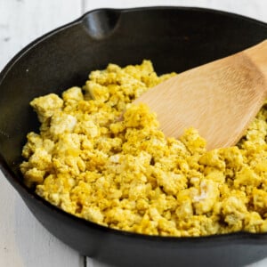 Easy vegan tofu scramble cooked in a cast iron skillet with serving spoon by sweet simple vegan blog