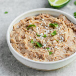 Side angle of Simple refried beans in a bowl topped with cheese and cilantro by Sweet Simple Vegan