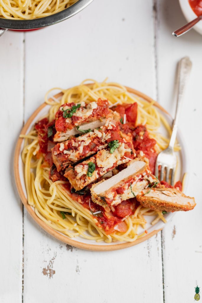 Slices of Vegan chicken parmesan garnished with basil on a plate with spaghetti, sweet simple vegan blog.