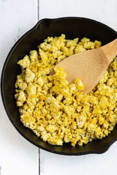 overhead photo of tofu scramble in cast iron skillet with wooden spatula