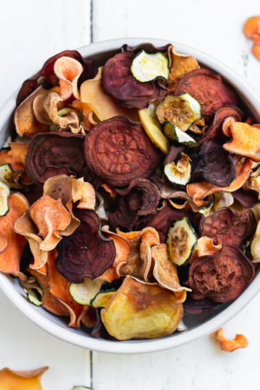 mixed vegetable chips in a bowl on a white background by sweet simple vegan
