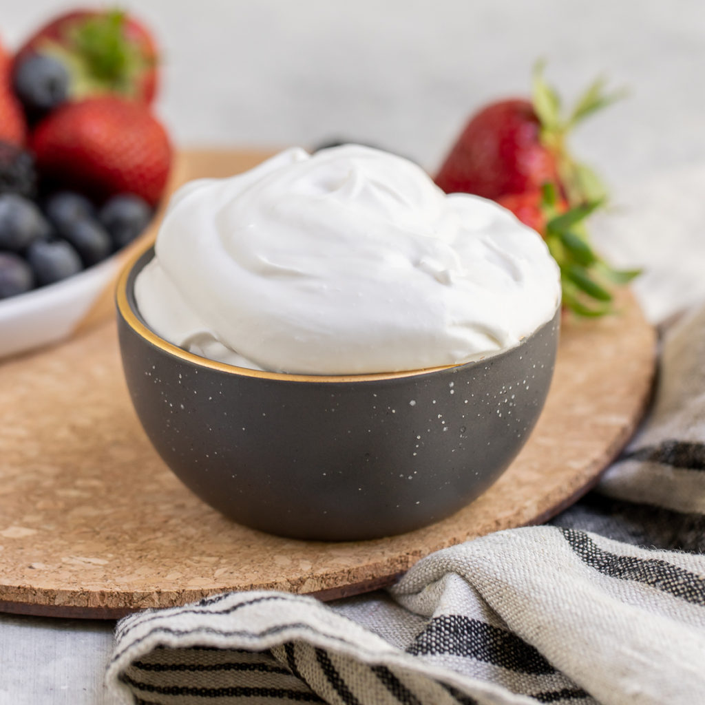 Bowl of fluffy coconut whipped cream next to berries by Sweet Simple Vegan