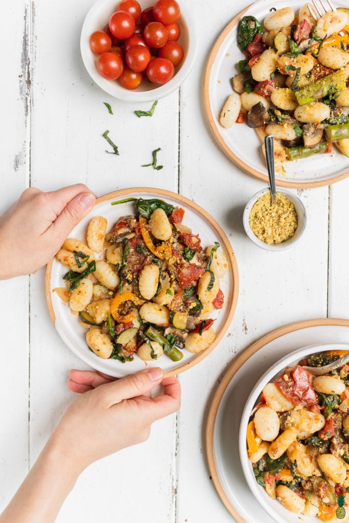 Hands holding Easy vegetable gnocchi dish in a bowl by sweet simple vegan