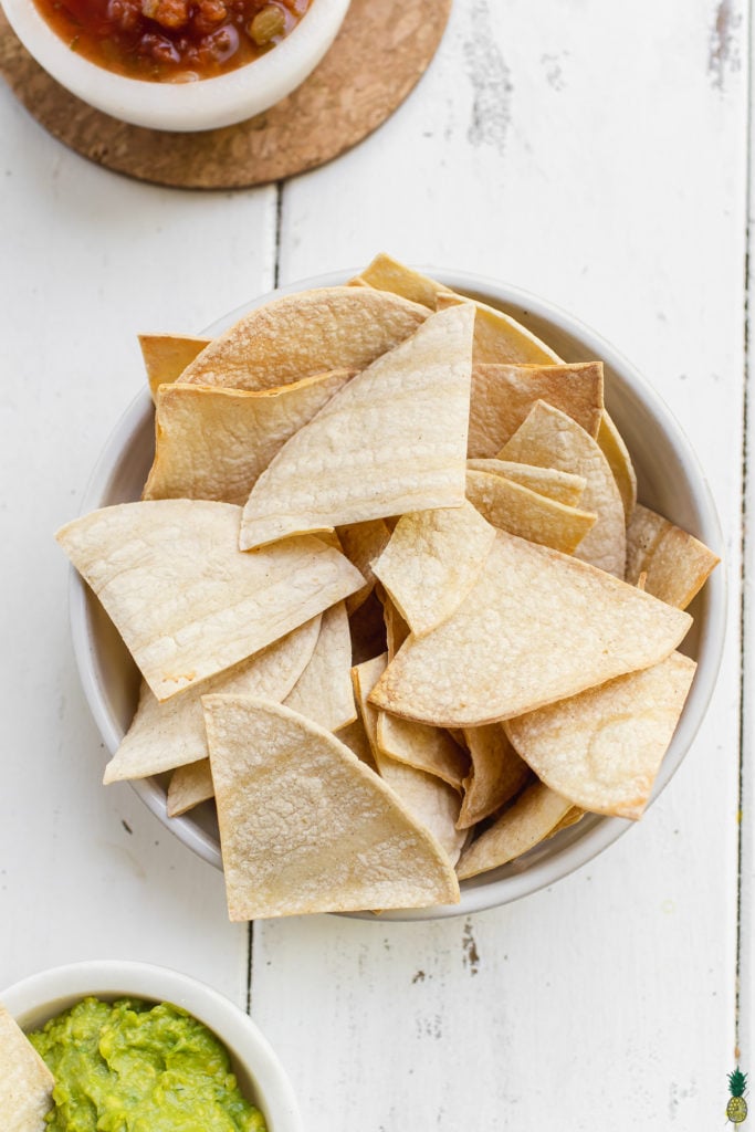 Homemade tortilla chips in a bowl with guacamole, salsa and lime