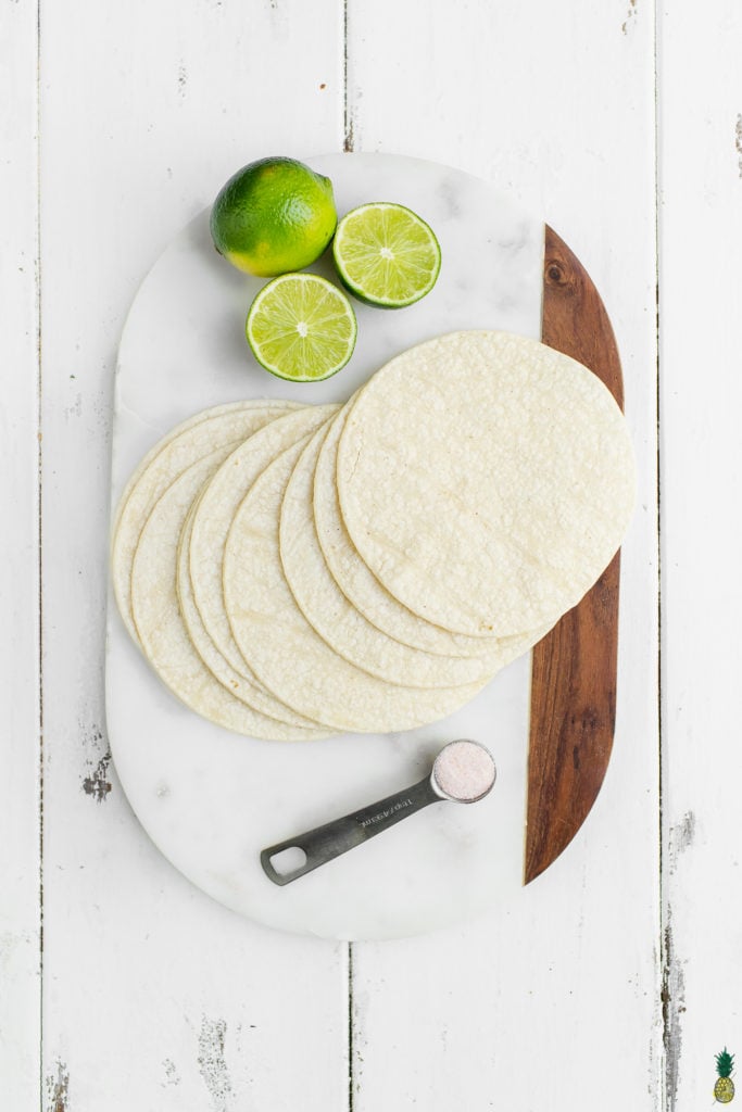 Tortillas, lime and salt on a marble board for homemade tortilla chips.