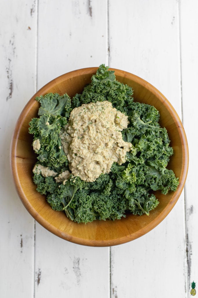 Curly kale in a large bowl covered in vegan ranch dressing for baked kale chips by sweet simple vegan