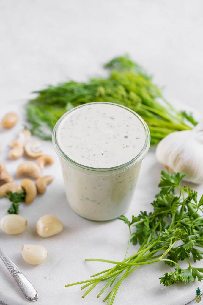 Cashew ranch dressing in a cup surrounded by ingredients by sweet simple vegan