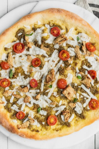 Close up shot of a vegan chicken pesto pizza with tomatoes by sweet simple vegan