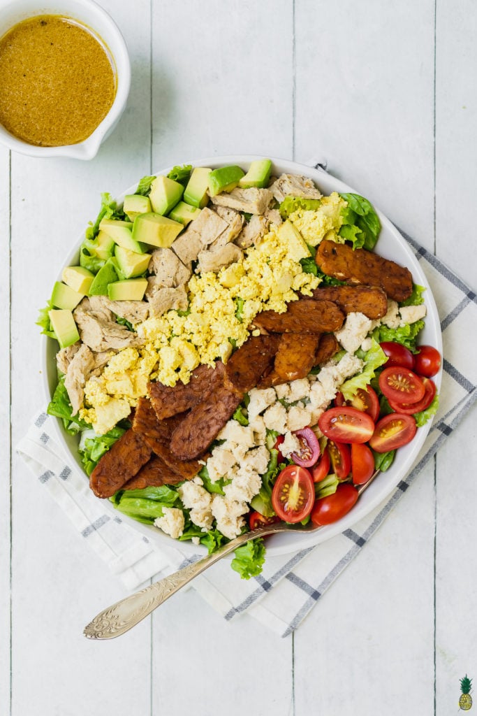 vegan cobb salad with tempeh bacon, tofu scramble, vegan feta cheese, vegan chicken and a vinaigrette on the side.