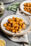 Vegan pumpkin gnocchi with sage butter sauce on a white plate with a fork and vegan parmesan cheese