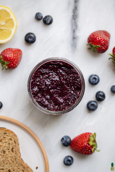 Chia seed jam in a jar surrounded by fresh berries, lemon and toast by sweet simple vegan