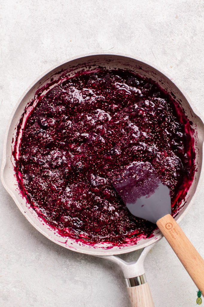 Step by step instructions on how to make chia seed jam at home; berries being cooked down in a gray pan.
