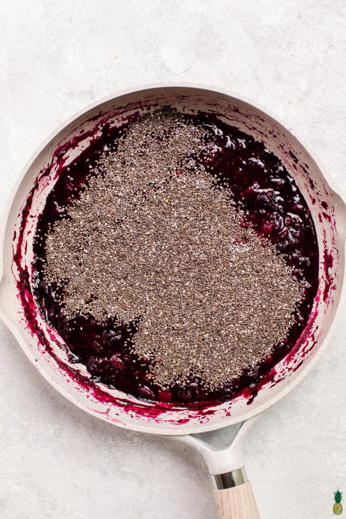 Step by step instructions on how to make chia seed jam at home; berries being cooked down in a gray pan.
