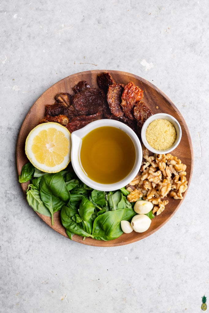 Ingredients to make vegan sun dried tomato pesto pasta on a wooden plate