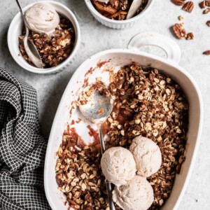 A tray of baked vegan apple crisp with two serving bowls and vanilla ice cream