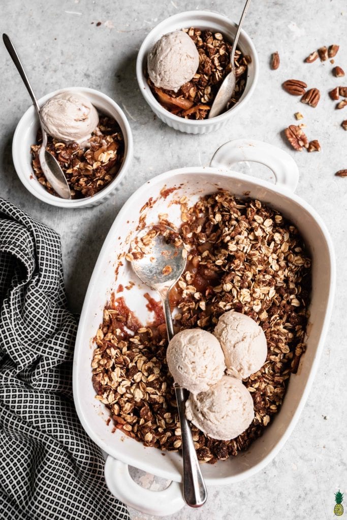 A tray of baked vegan apple crisp with two serving bowls and vanilla ice cream