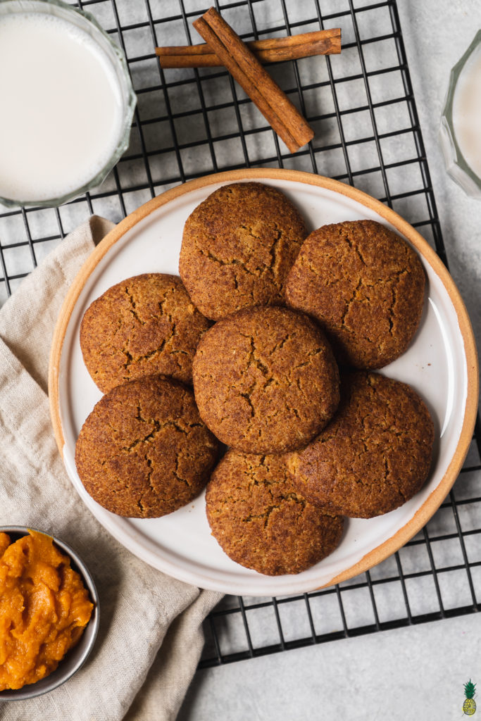 vegan gluten free pumpkin snickerdoodles on a plate with a cooling rack and almond milk