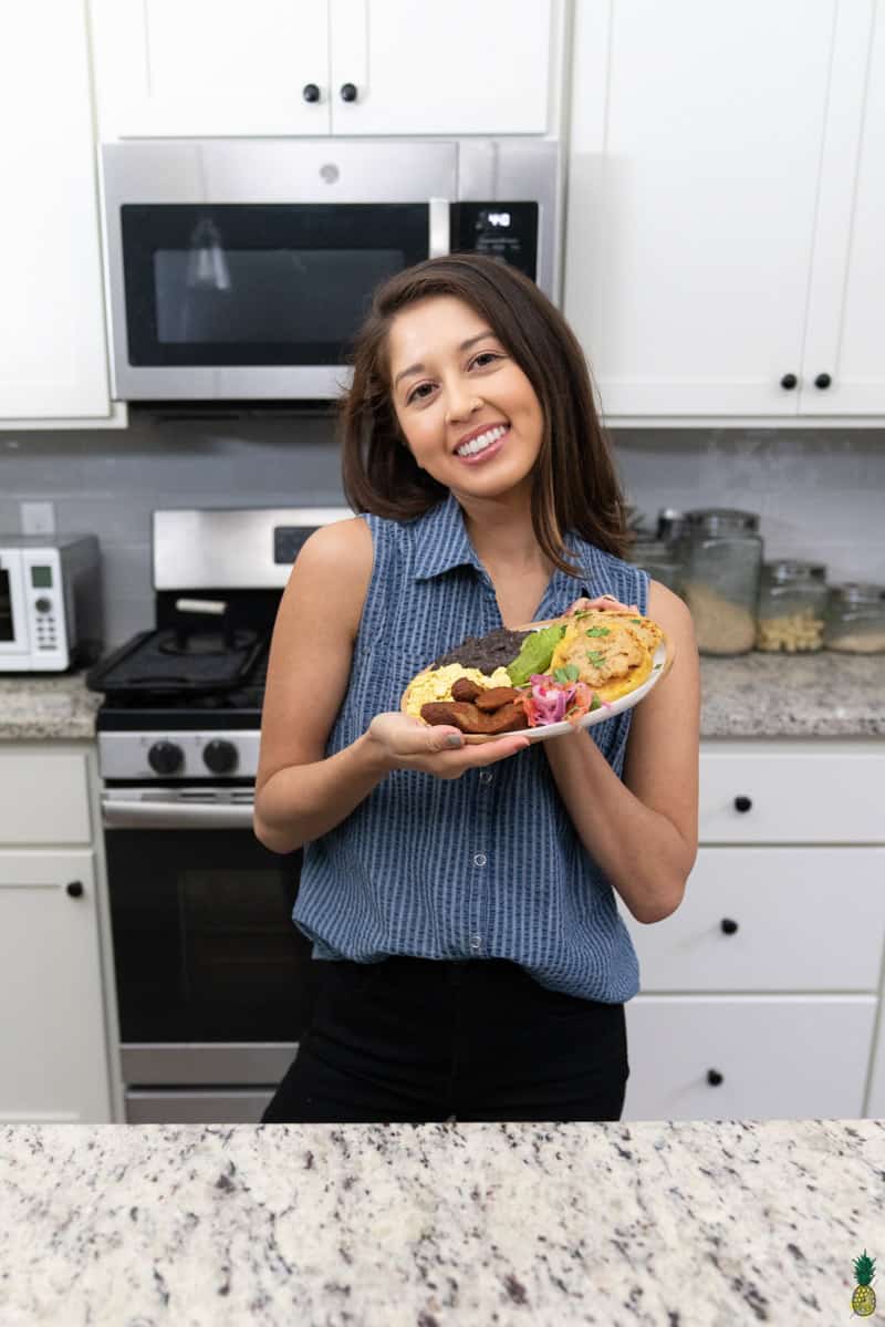 jasmine posing with a white plate of llapingachos, vegan eggs, curtido, salsa de maní, vegan chorizo and avocado