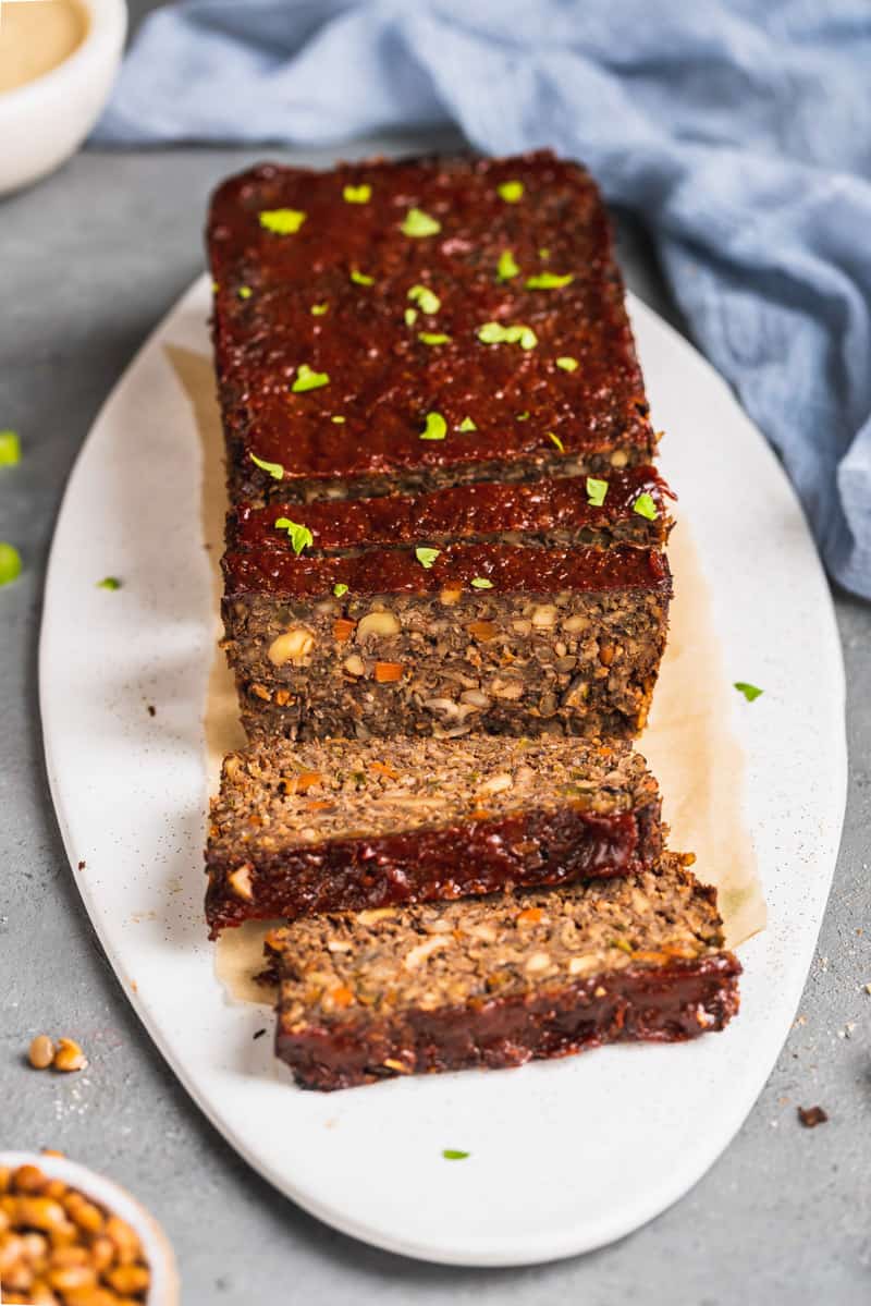 a close up shot a vegetable meatloaf with a ketchup topping on a white serving platter, surrounded by ingredients