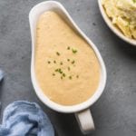 vegan gravy in a white gravy boat with chives and mashed potatoes on the side