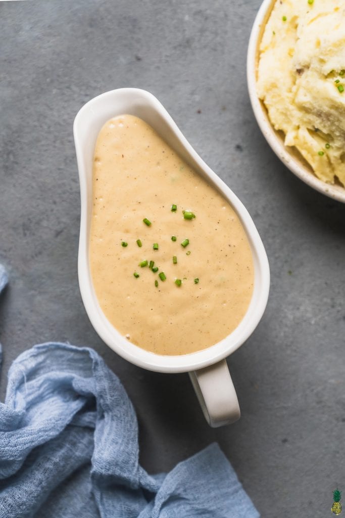 vegan gravy in a white gravy boat with chives and mashed potatoes on the side