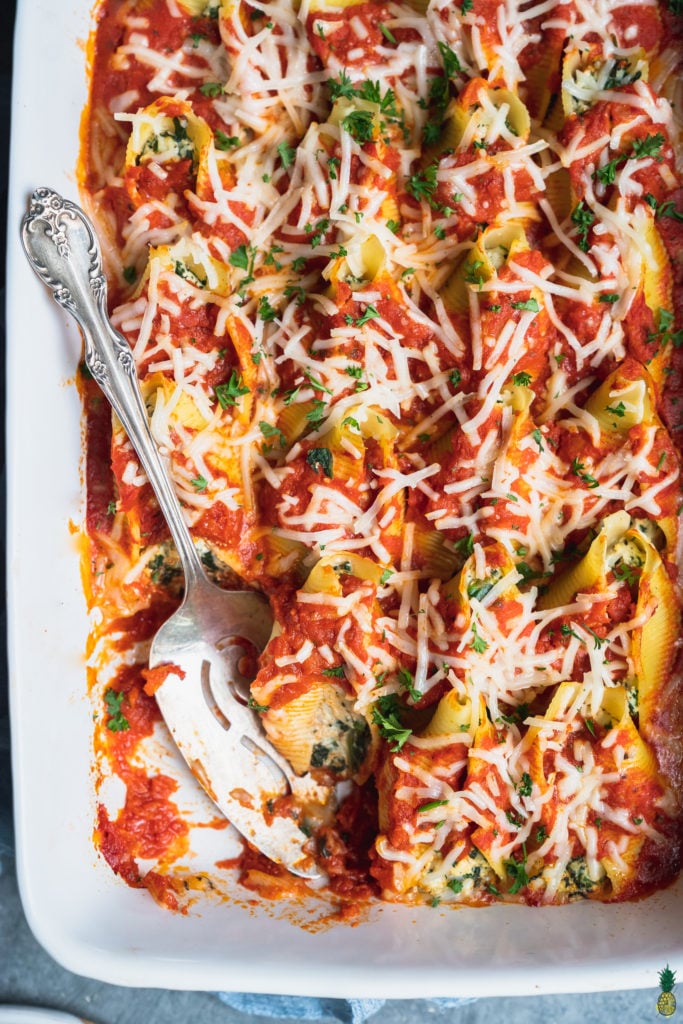 a close up shot of a vegan stuffed shells recipe with a scoop taken out of the baking dish