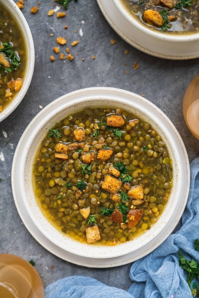 An overhead shot of a vegan lentil and split pea soup in a white bowl on a dark background by sweet simple vegan