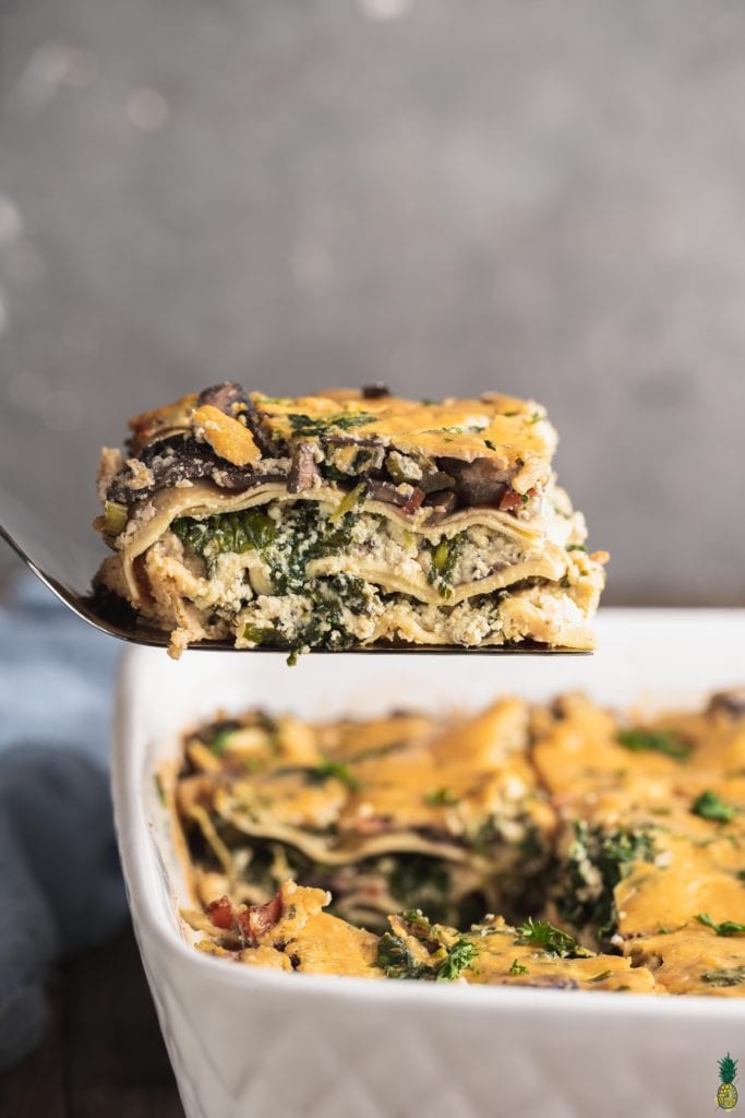 A cut slice of vegan white lasagna on a spatula being scooped out of the dish by sweet simple vegan