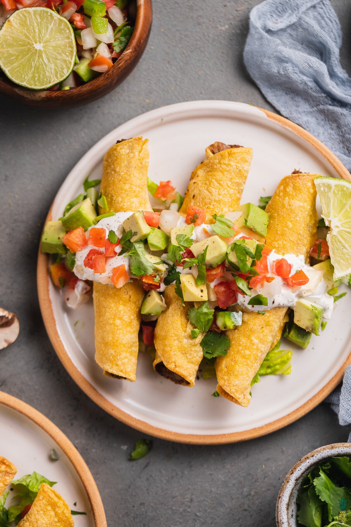 close up of a plate of mushroom potato taquitos with vegan sour cream, pico de gallo, avocado and lime